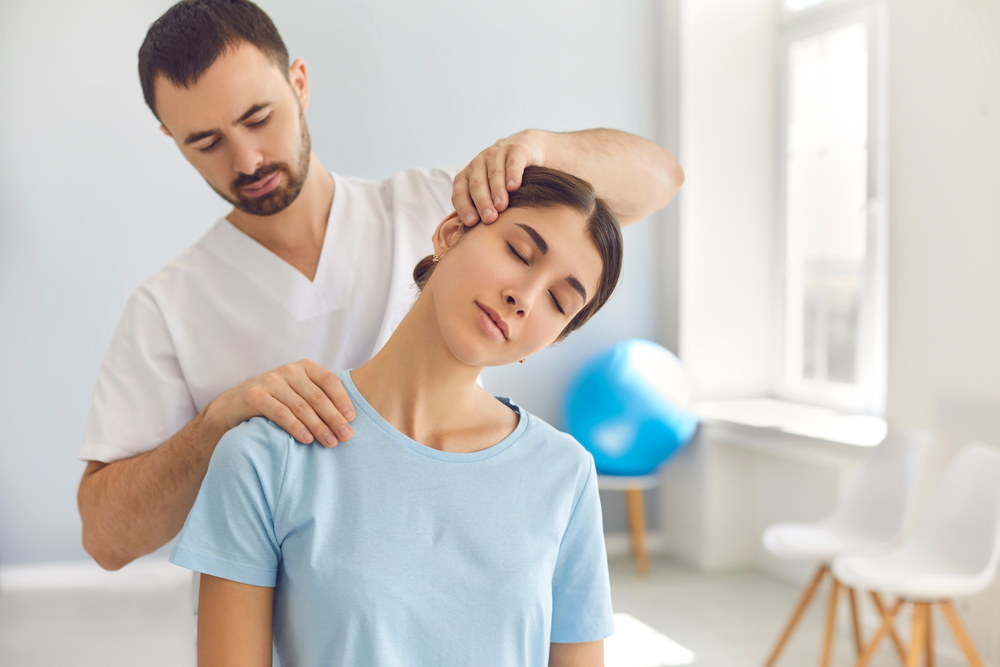 Licensed chiropractor or manual therapist doing neck stretch massage to relaxed female patient in clinic office