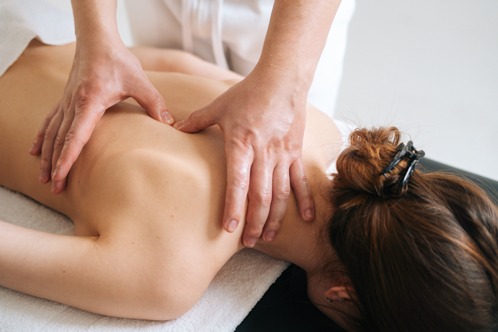 Massage therapist massaging young woman's back and shoulders while she lays on a massage table