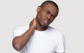 Man in white shirt rubs his neck in pain