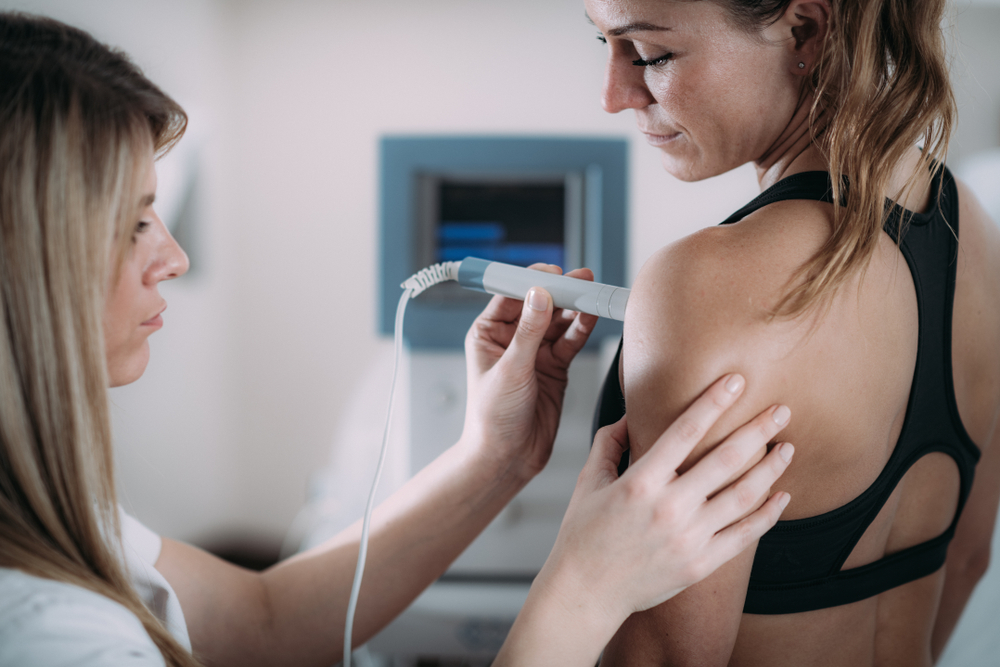 Physical therapist treats female patient's shoulder with a laser therapy wand