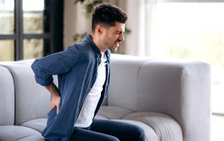 man on couch massaging his back, suffering from back pain