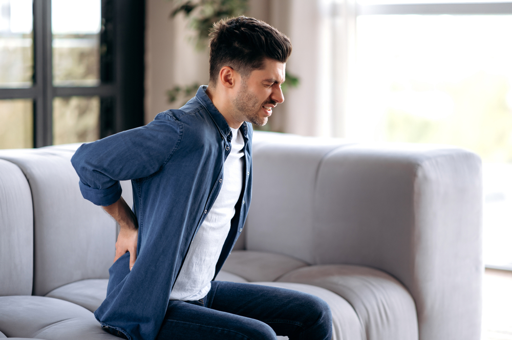 man on couch massaging his back, suffering from back pain