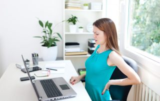 young woman having a back pain while sitting at the working desk