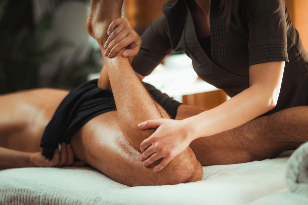 Physiotherapist massaging male patient with injured leg muscle