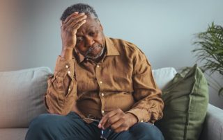 Senior man sitting on a couch holding his head and looking distressed or fatigued at home