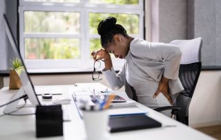 Woman sitting at desk experiencing lower back pain while working in office