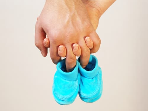 A person holds a pair of small blue baby shoes in one hand, symbolizing pregnancy, expecting a child, parenthood, family planning, or the arrival of a new baby.